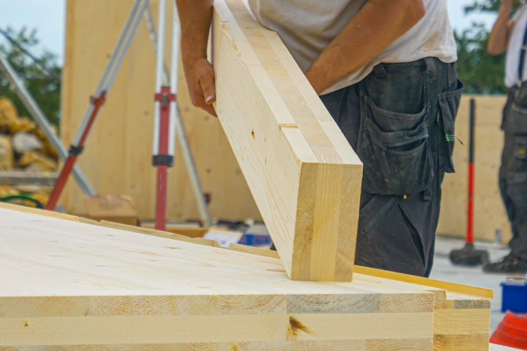 A builder lays an engineered wood beam on to wooden foundations.
