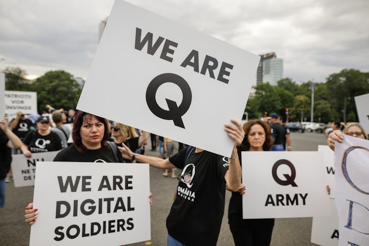 three white women holding signs that read WE ARE Q, Q ARMY and WE ARE DIGITAL SOLDIERS
