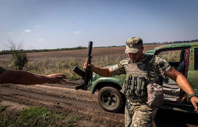A Ukrainian soldier hands an automatic rifle to a colleague