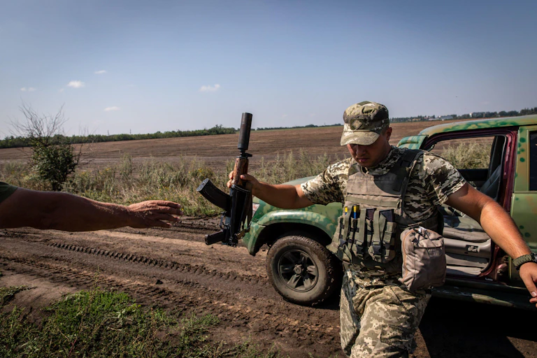 A Ukrainian soldier hands an automatic rifle to a colleague
