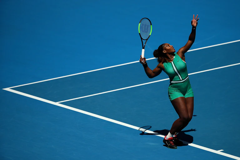 Female tennis player in green outfit throws ball into air during her serve.
