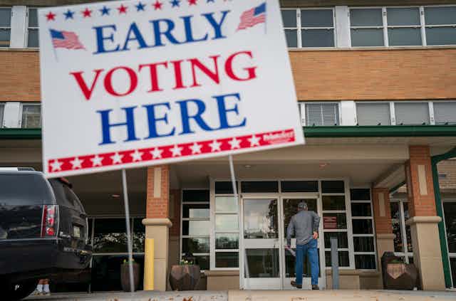 A person walks into a building where a large sign is hanging saying 'Early voting here'/