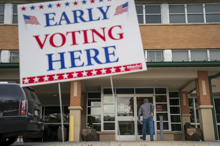 A person walks into a building where a large sign is hanging saying 'Early voting here'/