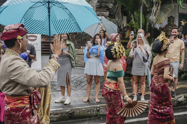 People take photographs of people marching in a parade.