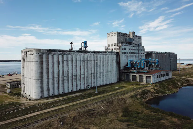 A large industrial building sits on a piece of land jutting out into the ocean