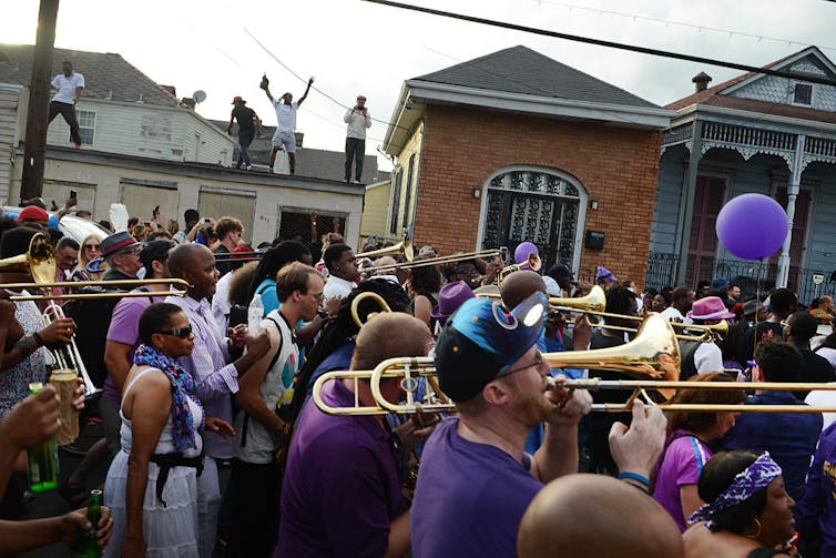 Locals wearing purple march through the streets playing instruments.