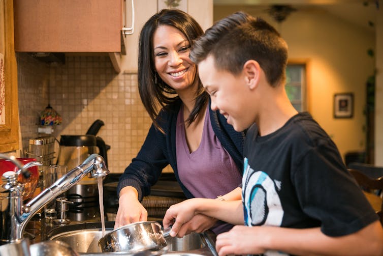A smiling woman and a boy washing dishes