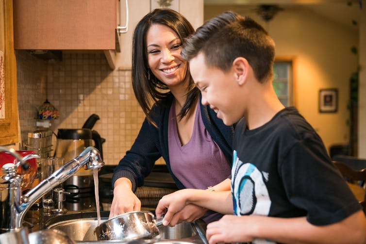 A smiling woman and a boy washing dishes