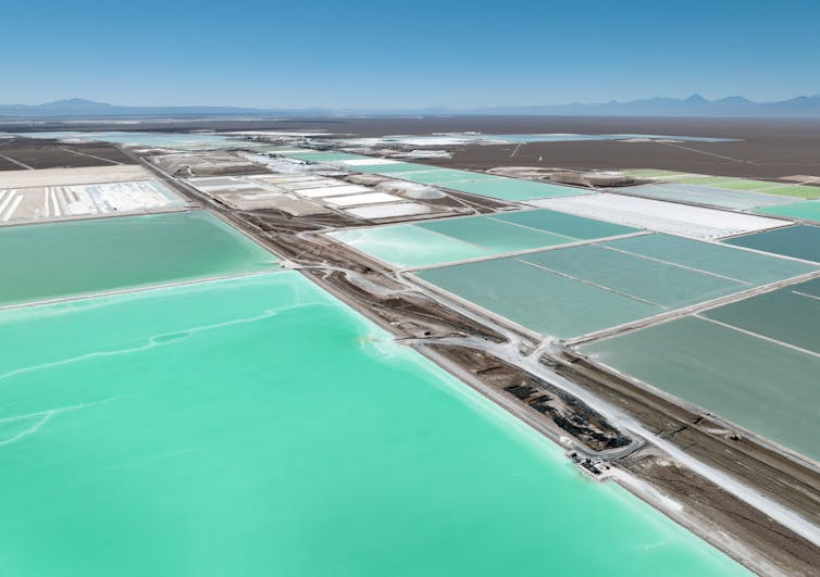 A field sectioned into rectangles with bright turquoise water or white salt stretches over several miles of otherwise empty landscape with mountains far in the distance.