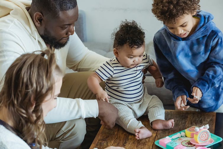 A man with two young children and a baby sit around a table.