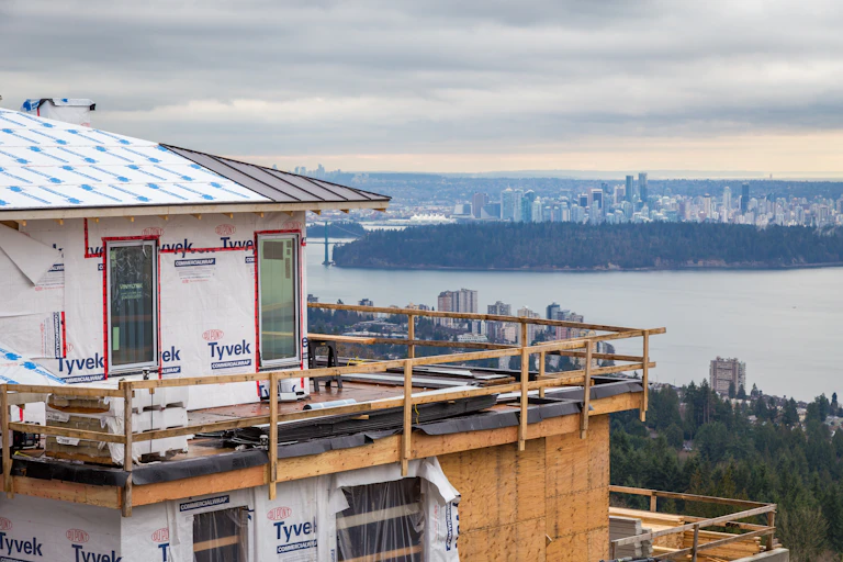 A house under construction is seen in the foreground. In the ground, a city skyline is visible