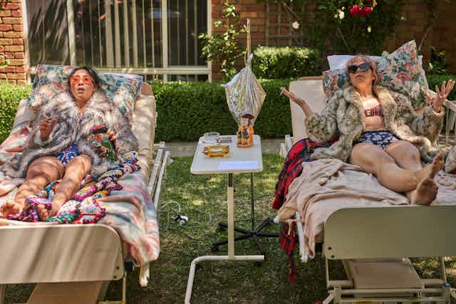 Two women sunbathe on hospital beds
