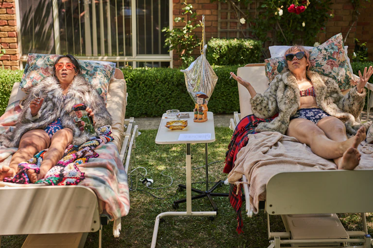 Two women sunbathe on hospital beds