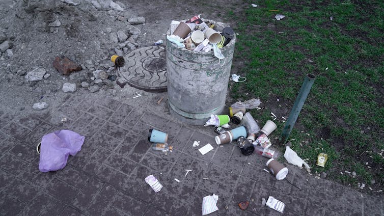 a public rubbish bin filled with PPE and surgical masks to the point of overflow