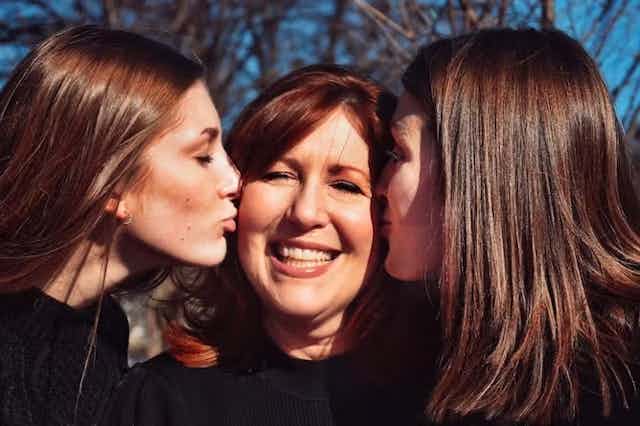 Dua anak perempuan dewasa mencium pipi ibu mereka
