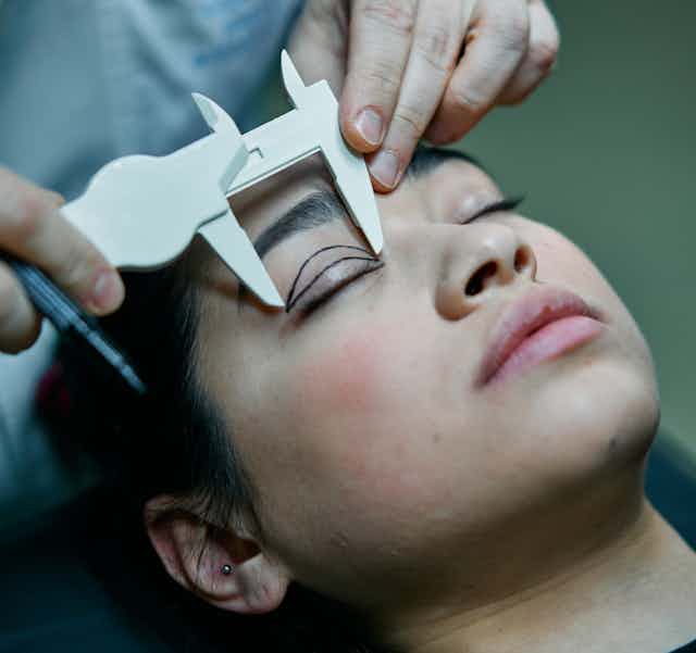 Cosmetic surgeon measuring eyelids ahead of surgery