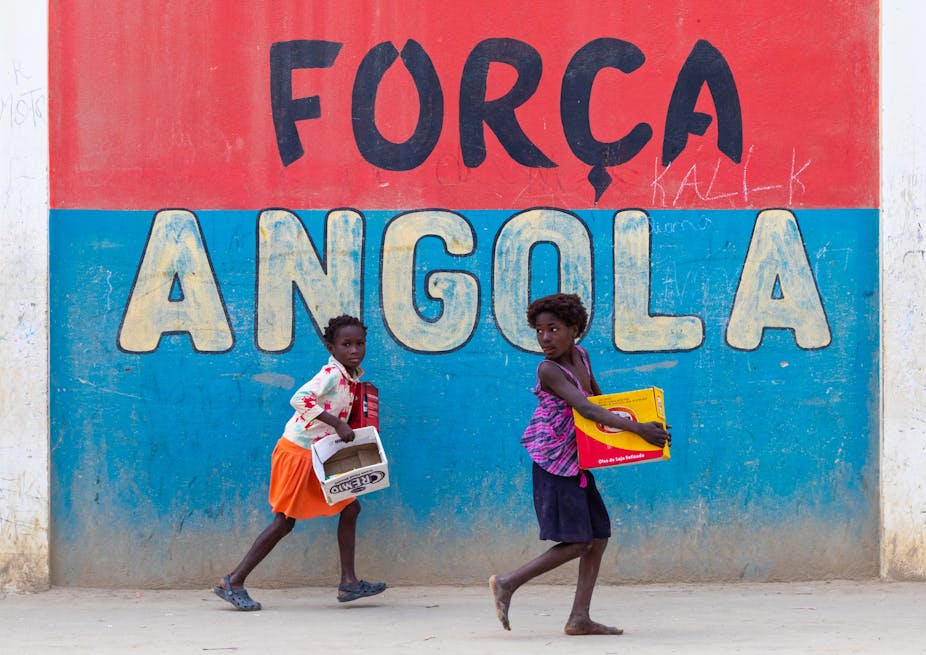 Angolan girls in front of a patriotic slogan on a wall.