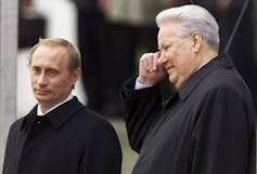 An aging man with grey hair stands next to a younger blonde man.