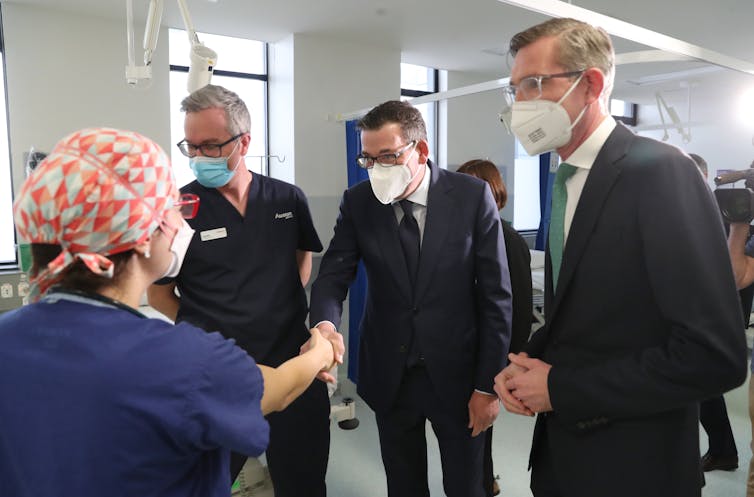 Victorian Premier Daniel Andrews (centre) greets a healthcare worker on Tuesday, during a visit with NSW Premier Dominic Perrottet.