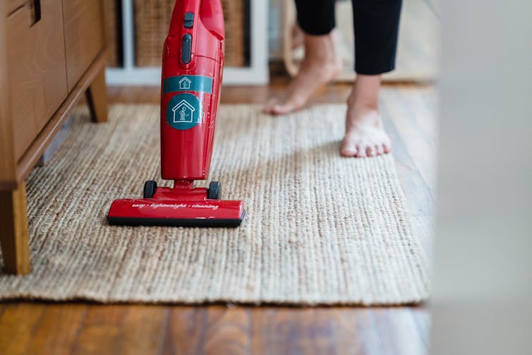 Person vacuuming a rug on a timber floor in the home