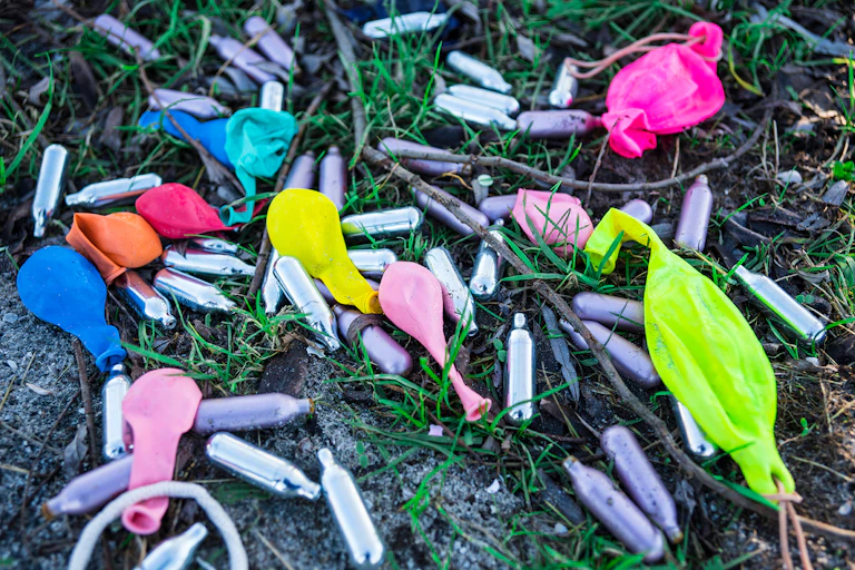 Photos de cartouches de gaz hilarant et de ballons de baudruches abandonnées dans l’herbe.