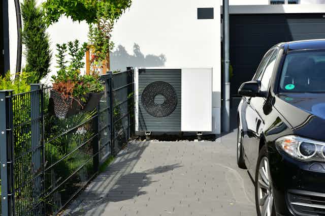 Heat pump at side of house next to garage and car