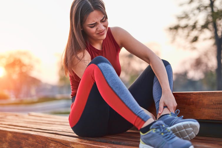 A young woman wearing athletic wear grips her ankle in pain.