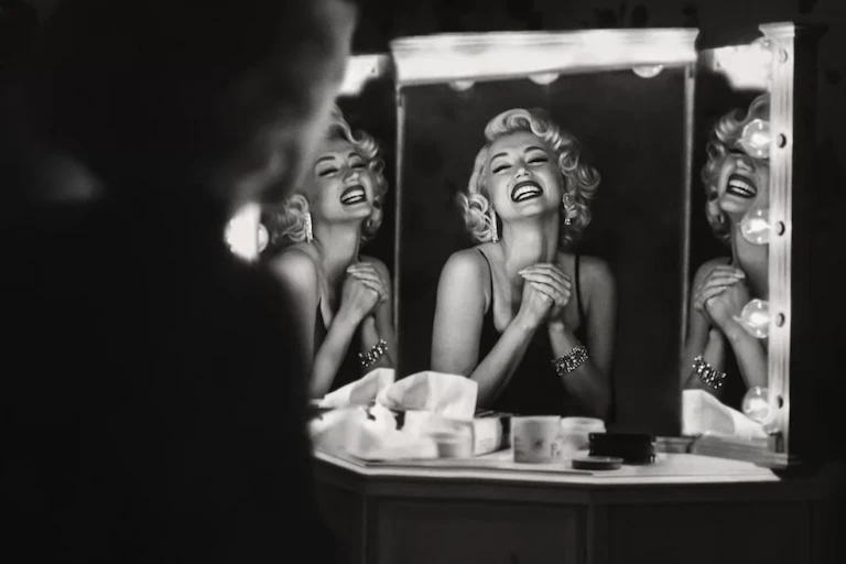 Blonde woman with eyes closed smiling before a mirror.