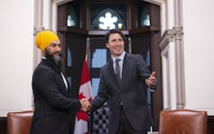 A man in a yellow turban shakes hands with another man. Both are smiling.