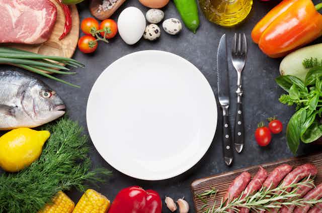 Une assiette blanche est entourée de produits crus susceptibles d'être contaminés : poisson, viande, œufs, légumes…
