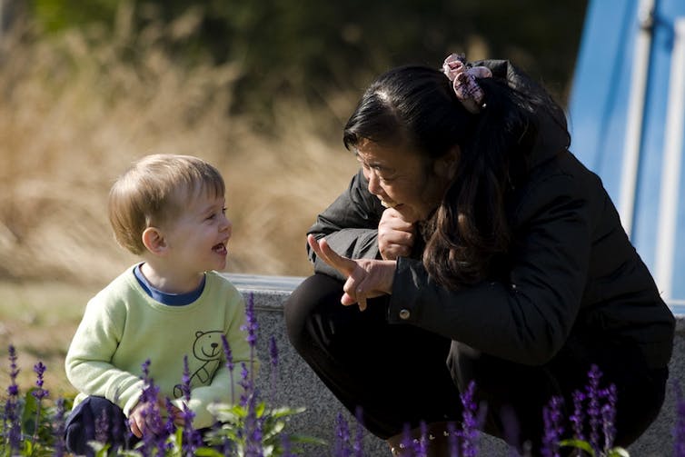 A woman seen holding up fingers to a toddler and talking with him.