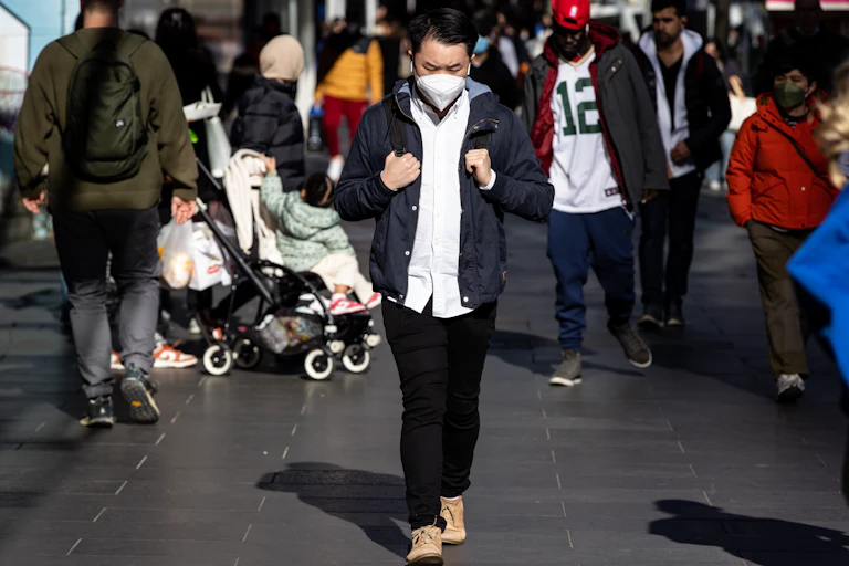 man walks on street with mask on and head down