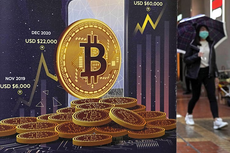 woman in mask walks past Bitcoin display