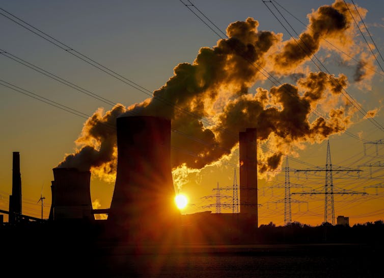 sun sets behind power plant emitting steam