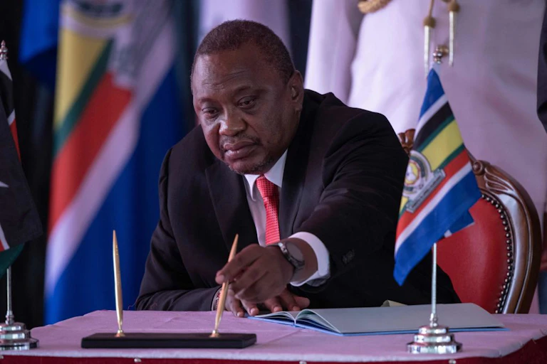 Man seating at a table with the East African Community flag in front of him.