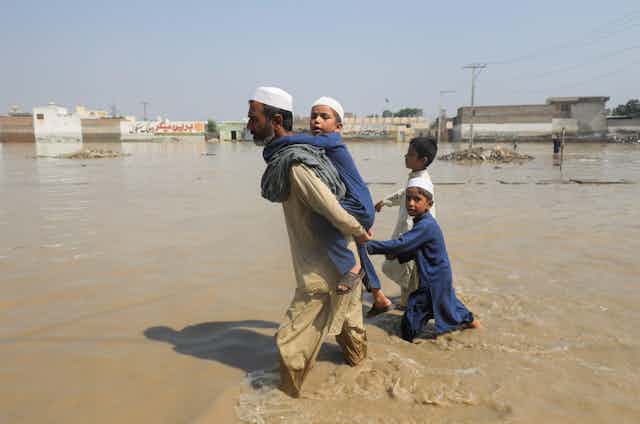 A man leading three children through flood waters.