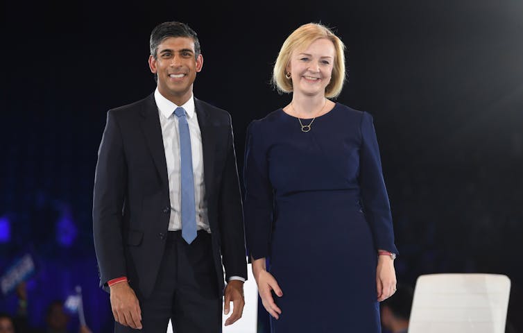 Rishi Sunak and Liz Truss smile and stand side by side on a stage after a campaign event