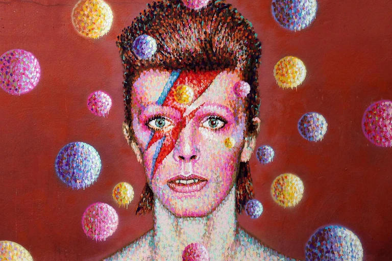 Retrato mural de David Bowie como Ziggy Stardust rodeado de esferas de colores sobre fondo rojo.