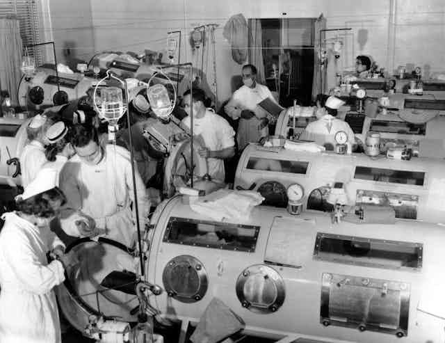 Critical-care patients are lined up close together in iron lung respirators