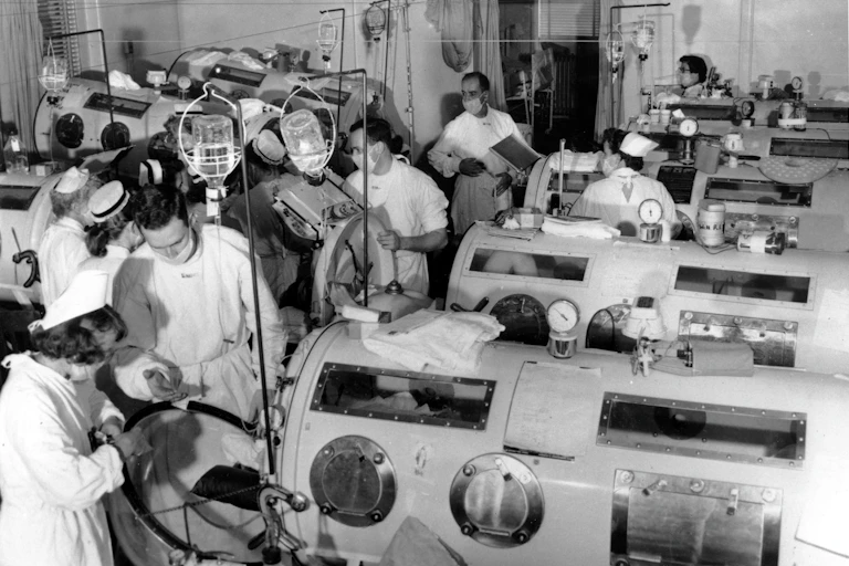 Critical-care patients are lined up close together in iron lung respirators