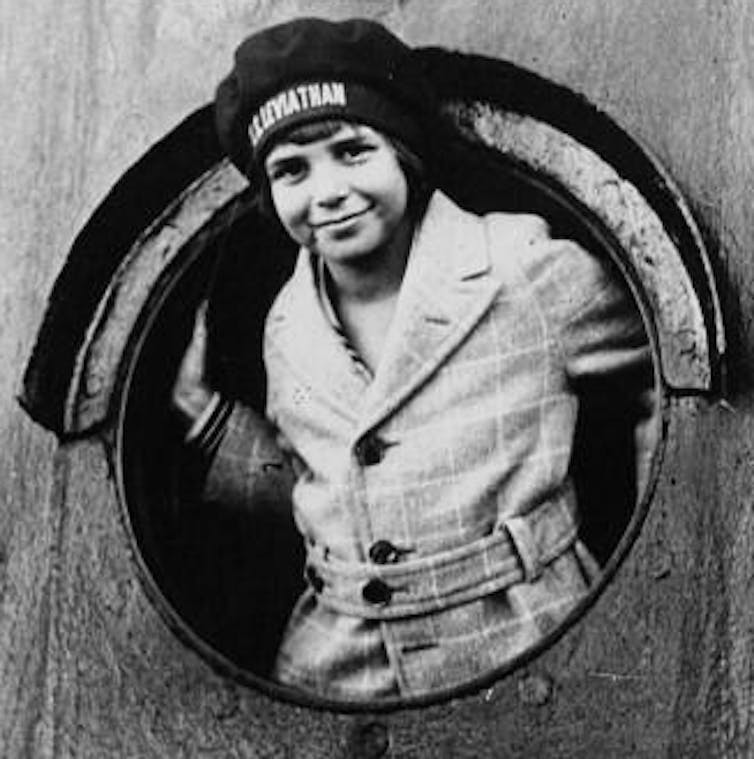 A black and white photo of a young boy looking out of a ship window.