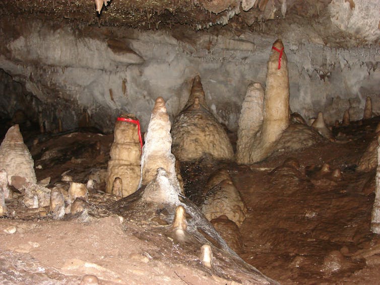 A photo from inside a cave, with red ribbons tied around two different stalagmites.