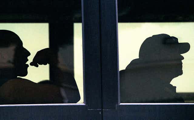 Silhouettes of two baseball players through bus windows.
