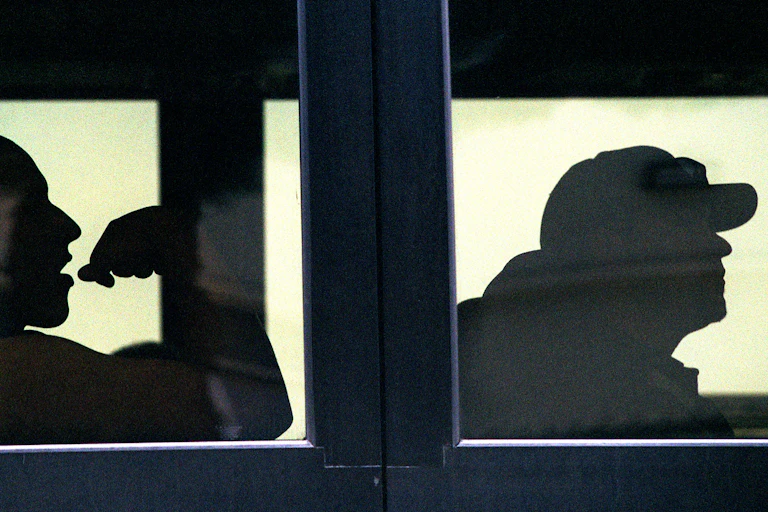 Silhouettes of two baseball players through bus windows.