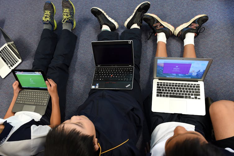 Three students sit with laptops in their laps.