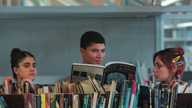 Three teens behind library shelves.