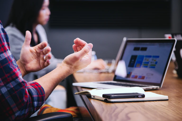 a man's hands explaining something, in front of a laptop, a woman in the background