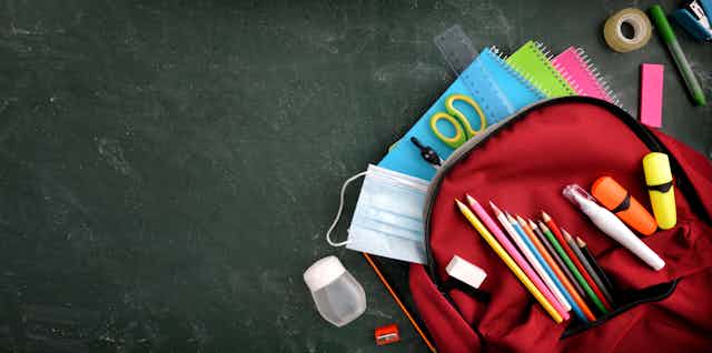 Un cartable ouvert laisse voir crayons de couleur, cahiers, ciseaux, scotch, gomme, colle, etc.