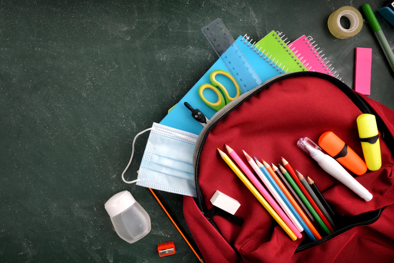 Un cartable ouvert laisse voir crayons de couleur, cahiers, ciseaux, scotch, gomme, colle, etc.