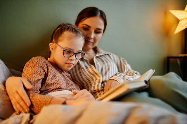 Photo d’une mère qui lit un livre avec sa fille atteinte de trisomie 21.